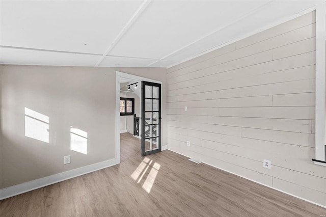 empty room featuring wooden walls, wood finished floors, baseboards, and french doors