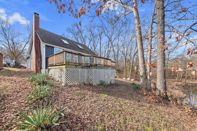 rear view of house with a chimney, a wooden deck, and roof with shingles