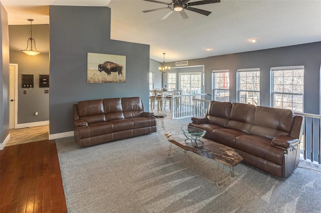 living area with vaulted ceiling, wood finished floors, ceiling fan with notable chandelier, and baseboards