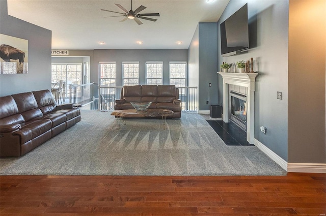 living area with a fireplace, a ceiling fan, baseboards, and wood finished floors