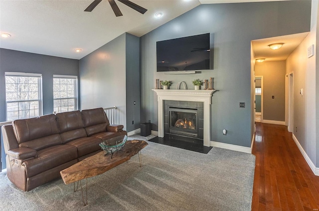 living room with lofted ceiling, a tiled fireplace, wood finished floors, baseboards, and ceiling fan