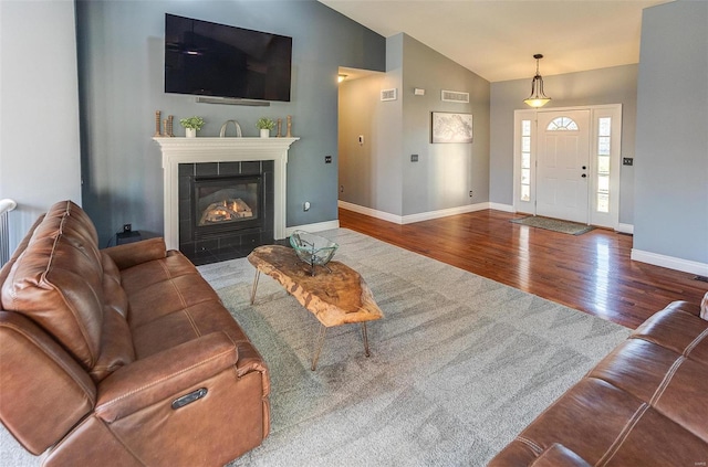 living area featuring visible vents, baseboards, vaulted ceiling, a fireplace, and wood finished floors