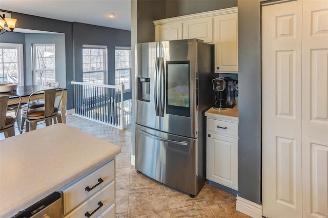 kitchen with white cabinetry, stainless steel fridge, light countertops, light tile patterned floors, and baseboards