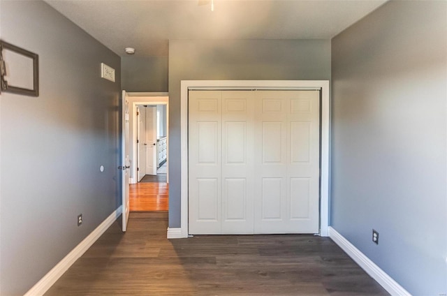 unfurnished bedroom featuring a closet, baseboards, and dark wood-style flooring