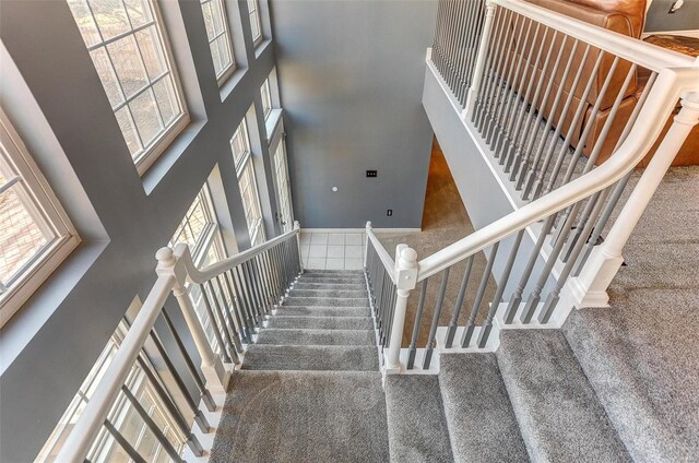 stairway featuring baseboards, plenty of natural light, carpet, and a towering ceiling