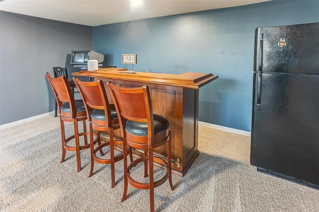 bar featuring carpet flooring, a dry bar, freestanding refrigerator, and baseboards