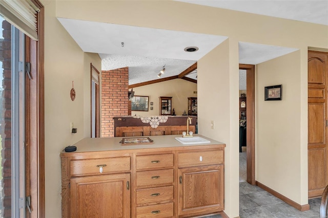 kitchen with a sink, a textured ceiling, a peninsula, light countertops, and vaulted ceiling