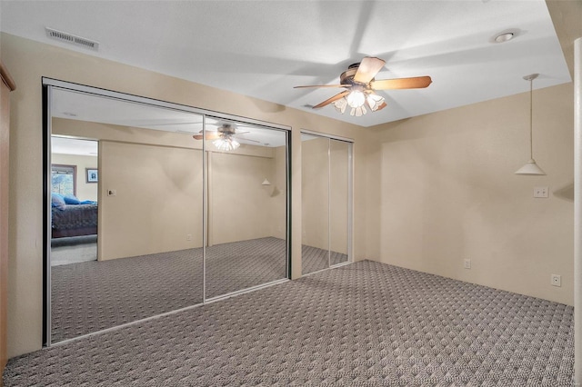 unfurnished bedroom with visible vents, two closets, a ceiling fan, and carpet