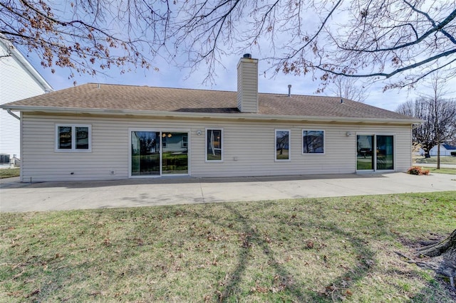 back of house with a patio, a lawn, a chimney, and a shingled roof