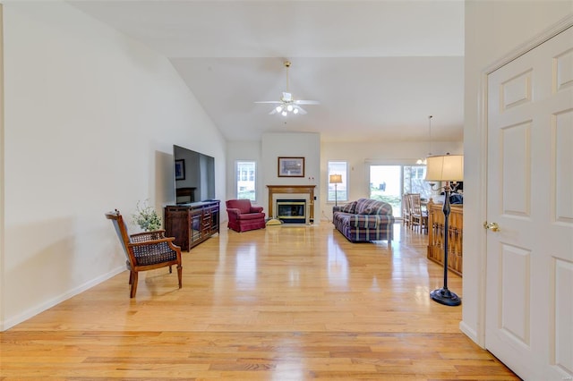 living room with a ceiling fan, baseboards, high vaulted ceiling, light wood-style floors, and a glass covered fireplace