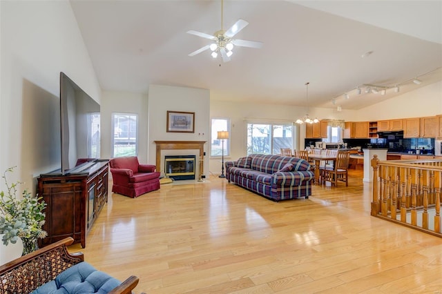 living room with a fireplace with flush hearth, light wood-style flooring, high vaulted ceiling, and ceiling fan with notable chandelier