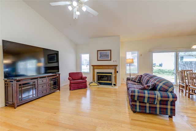 living room featuring a wealth of natural light, a glass covered fireplace, lofted ceiling, and light wood-style floors