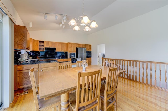 dining space with a notable chandelier, visible vents, light wood-style floors, and vaulted ceiling