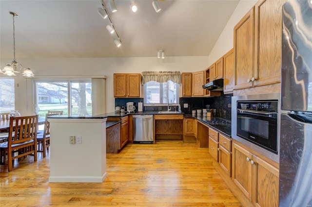 kitchen with a sink, under cabinet range hood, stainless steel appliances, a peninsula, and brown cabinetry