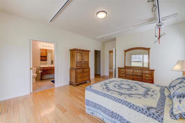 bedroom with light wood finished floors, connected bathroom, and baseboards