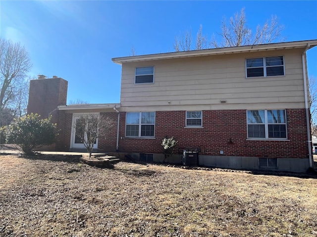 back of property featuring brick siding, central AC unit, and a chimney