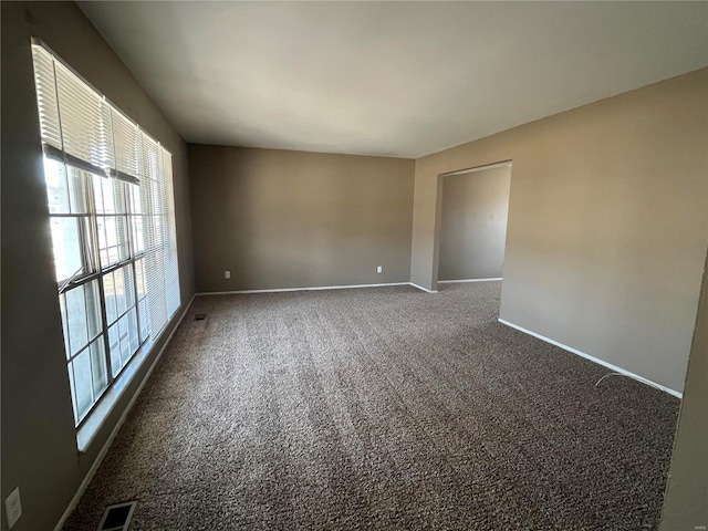 spare room with visible vents, baseboards, and dark carpet