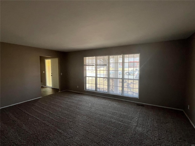 empty room with dark colored carpet, visible vents, and baseboards