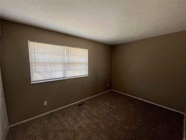 empty room featuring visible vents, dark carpet, and baseboards