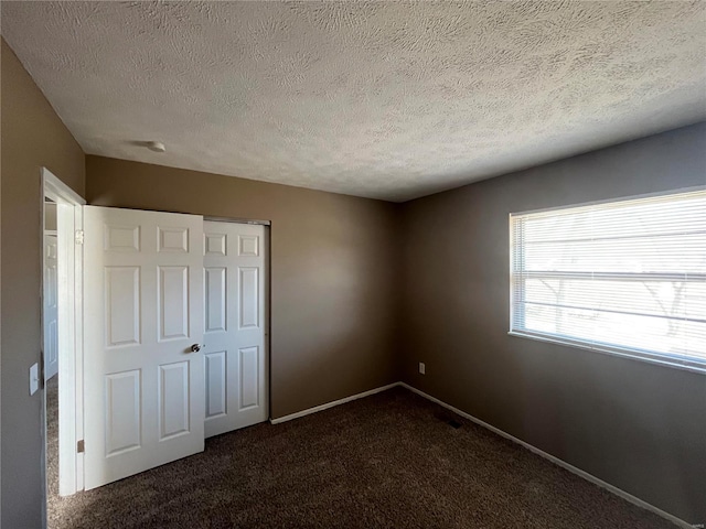 unfurnished bedroom with baseboards, a closet, dark carpet, and a textured ceiling