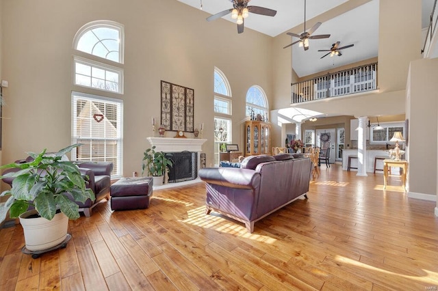 living area featuring a wealth of natural light, decorative columns, a fireplace with raised hearth, and light wood finished floors