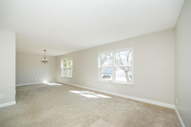 unfurnished room with a chandelier, light colored carpet, and baseboards