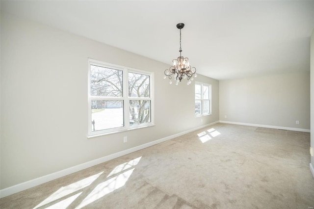 carpeted empty room featuring an inviting chandelier and baseboards