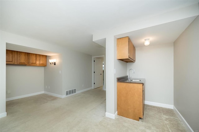 kitchen featuring light colored carpet, brown cabinetry, visible vents, and a sink