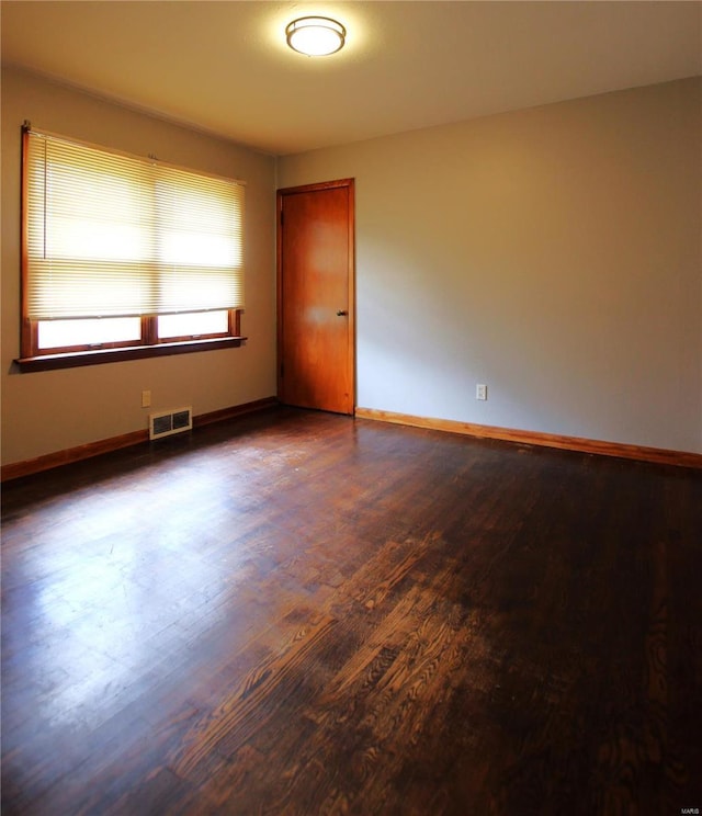 spare room with visible vents, baseboards, and dark wood-style floors