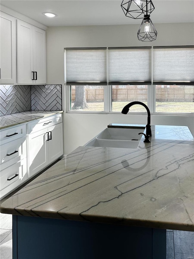 kitchen featuring light stone countertops, a sink, hanging light fixtures, white cabinets, and backsplash