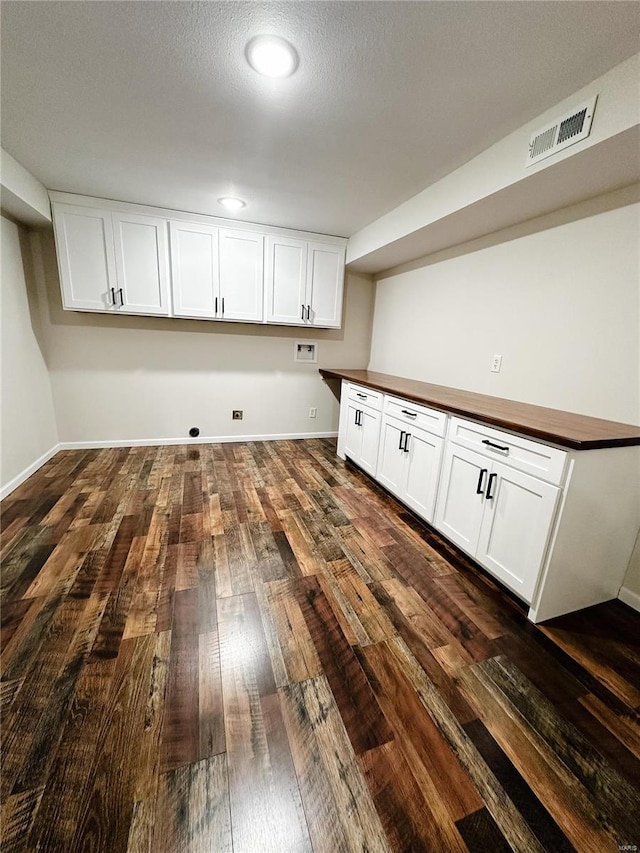 washroom with dark wood-type flooring, cabinet space, visible vents, and baseboards