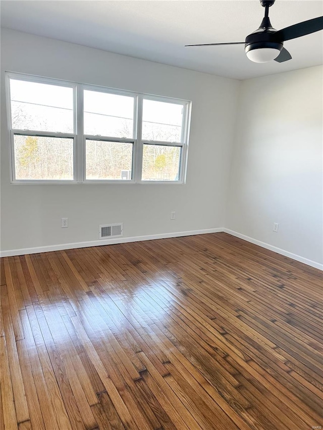 unfurnished room with ceiling fan, visible vents, baseboards, and dark wood finished floors