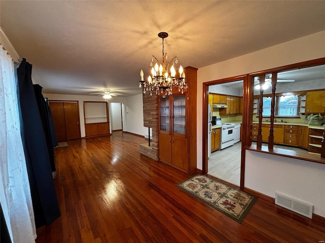 unfurnished dining area with visible vents, baseboards, ceiling fan with notable chandelier, wood finished floors, and a textured ceiling