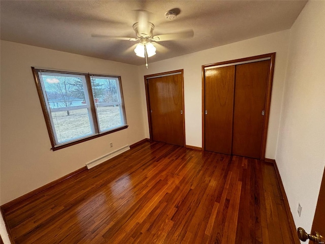 unfurnished bedroom with wood finished floors, baseboards, a baseboard radiator, ceiling fan, and multiple closets