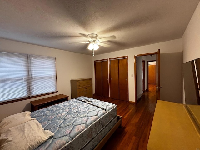 bedroom featuring multiple closets, dark wood-type flooring, a ceiling fan, and a textured ceiling