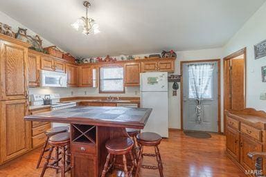 kitchen with a center island, a breakfast bar, light wood-style floors, a notable chandelier, and white appliances