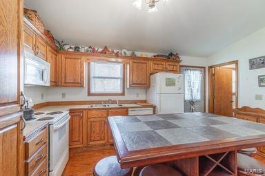 kitchen featuring tile countertops, lofted ceiling, brown cabinetry, white appliances, and a sink