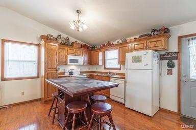 kitchen with light wood finished floors, a kitchen island, tile counters, vaulted ceiling, and white appliances