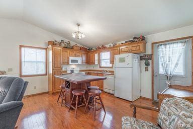 kitchen featuring light wood finished floors, a center island, open floor plan, vaulted ceiling, and white appliances