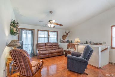 living room featuring ceiling fan, wood finished floors, and vaulted ceiling