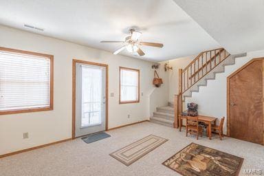 carpeted entryway featuring stairway, baseboards, and a ceiling fan