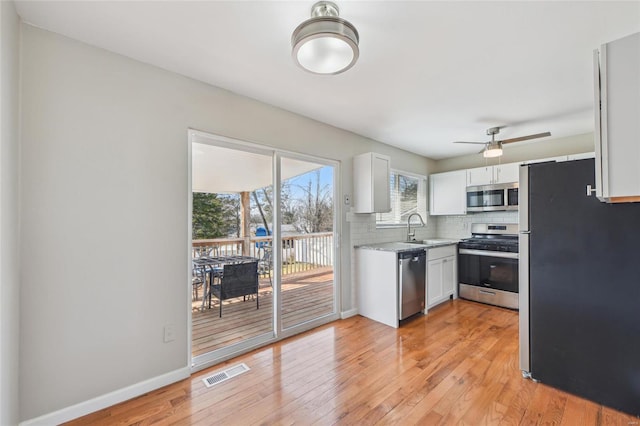 kitchen featuring visible vents, stainless steel appliances, light wood-style floors, white cabinets, and decorative backsplash