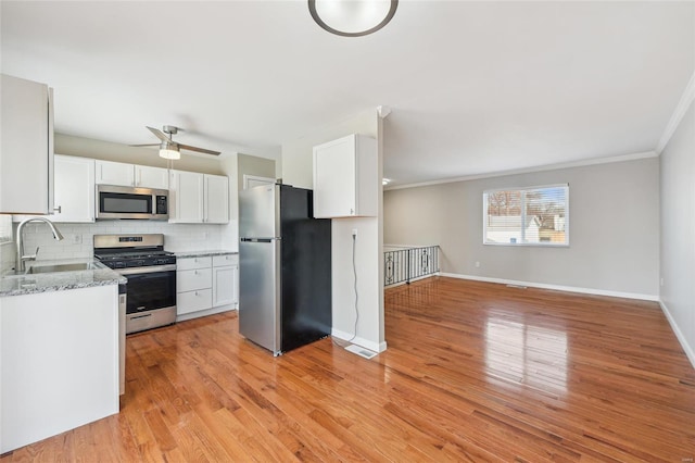 kitchen with tasteful backsplash, white cabinets, light wood finished floors, and stainless steel appliances