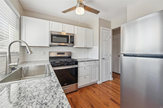 kitchen with a ceiling fan, a sink, appliances with stainless steel finishes, white cabinets, and light wood finished floors