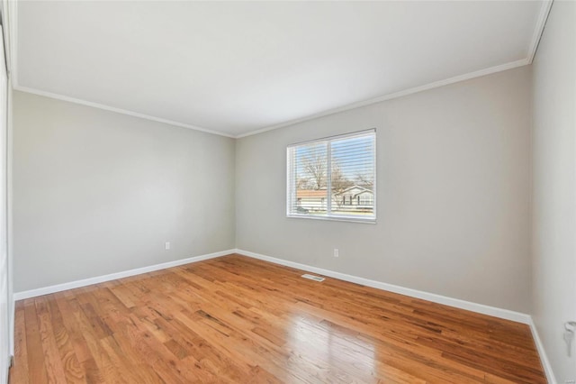 spare room featuring light wood-style floors, crown molding, visible vents, and baseboards