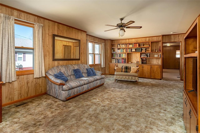 carpeted living room with visible vents, wood walls, crown molding, and ceiling fan