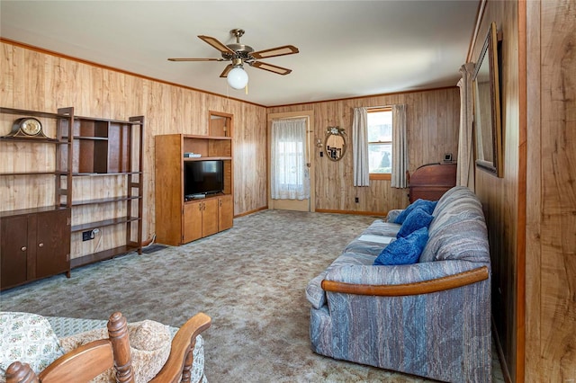 living area featuring ornamental molding, a ceiling fan, carpet, wood walls, and baseboards