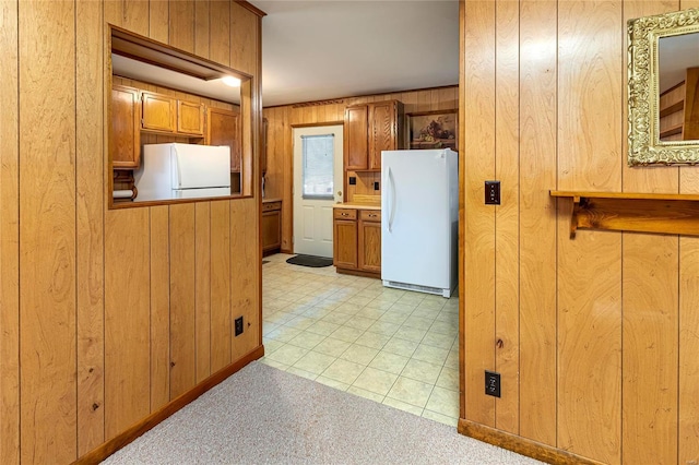 kitchen with brown cabinets, light carpet, wood walls, and freestanding refrigerator