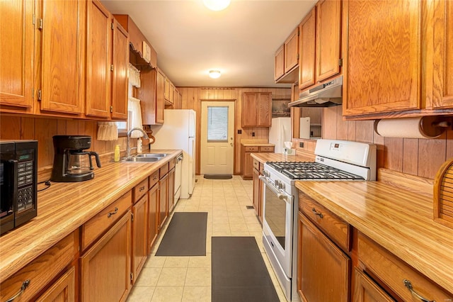 kitchen featuring butcher block countertops, under cabinet range hood, range with gas cooktop, brown cabinetry, and black microwave