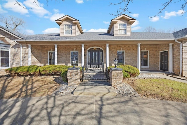 view of front of home with brick siding, a porch, and roof with shingles